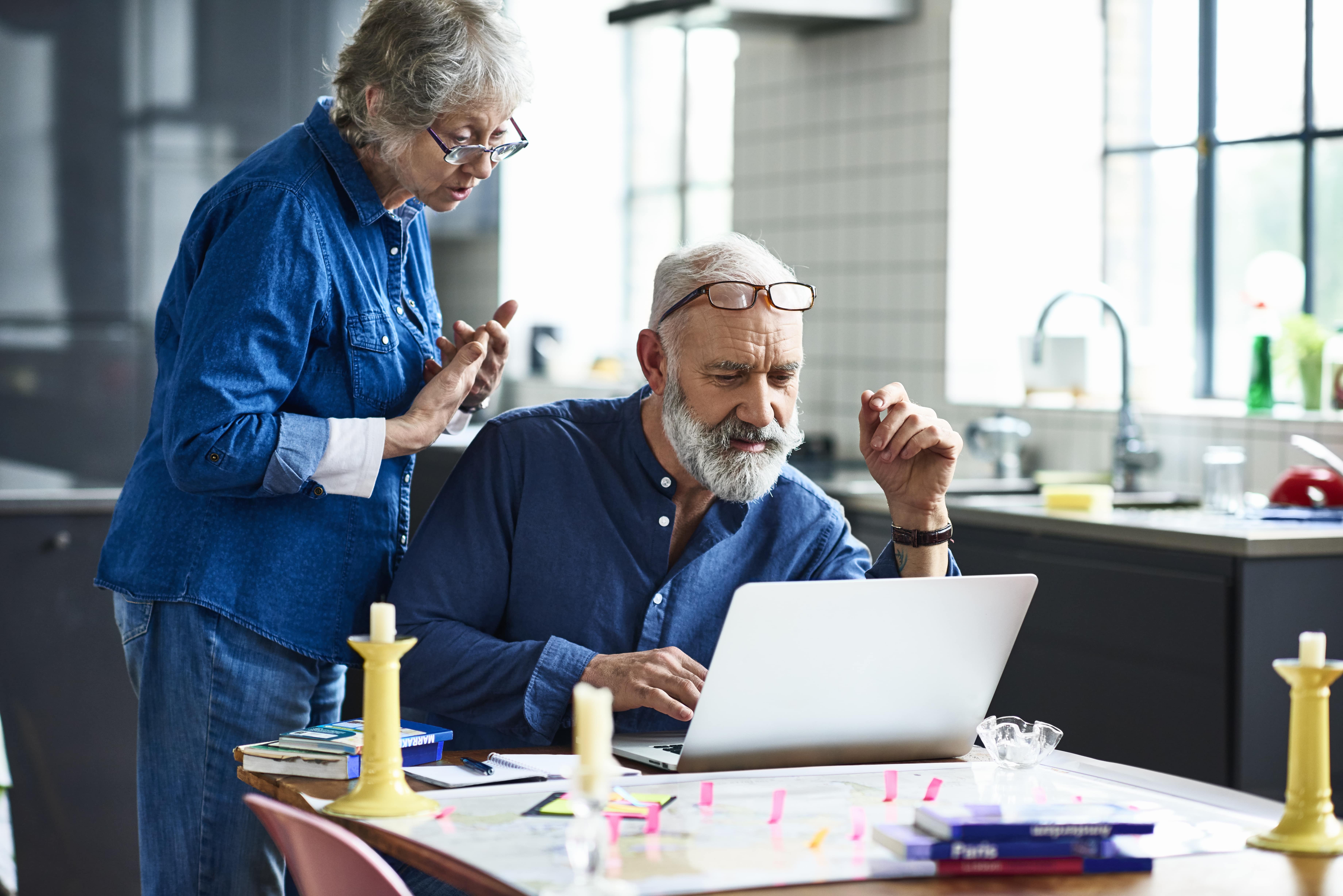 Senior man using laptop and woman watching over shoulder