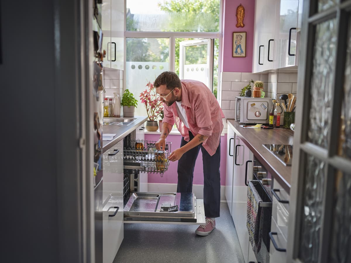 Man loading a dishwasher in a bright, modern kitchen, illustrating simple everyday ways to reduce energy use at home.