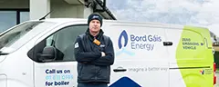 Person in outdoor workwear standing with arms folded beside a Bord Gáis Energy van.
