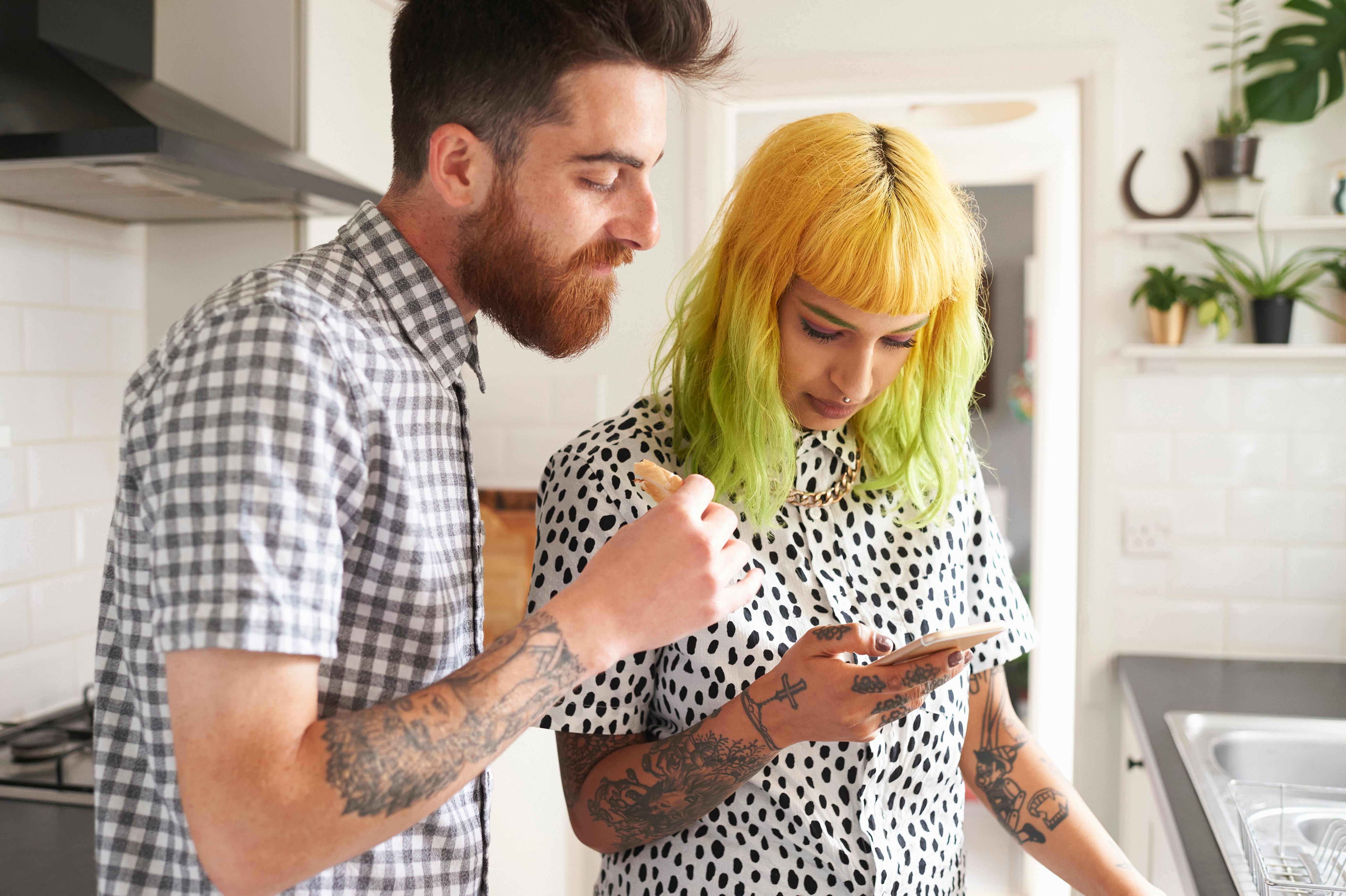 Young hipster couple looking at a smart phone in their kitchen
