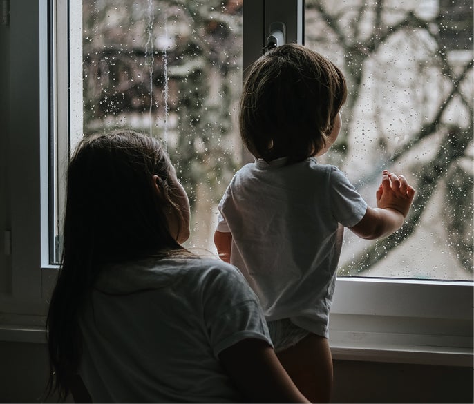 Mother and young child looking out rainy window