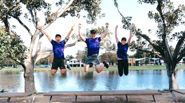 Tony, Andy and Tami jumping in Luminary t-shirts in front of the Yarra river