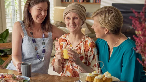 Three women laughing, the one in the middle wearing a scarf on her head. 