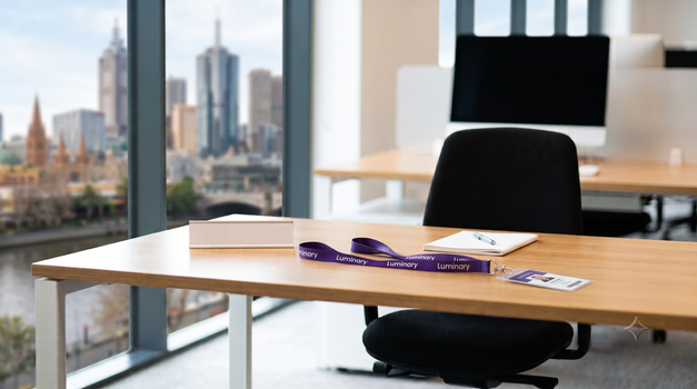 A desk set up and waiting for a new starter, with a Luminary lanyard, overlooking Melbourne. Generated by Gemini.