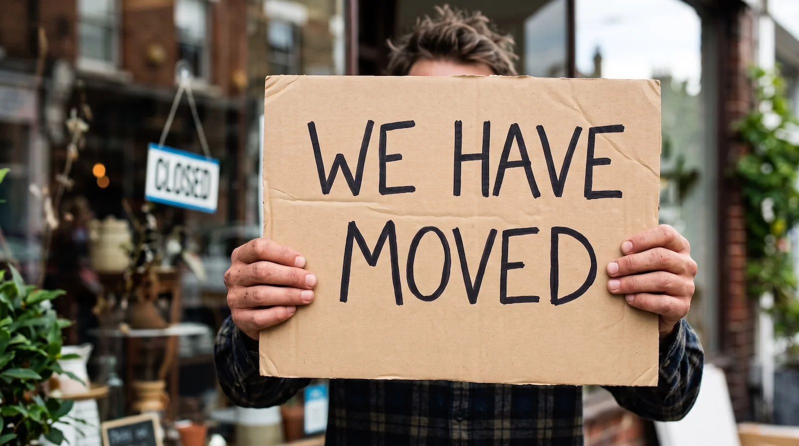 Picture of a man holding a sign that says 'We have moved'