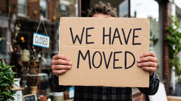 Picture of a man holding a sign that says 'We have moved'