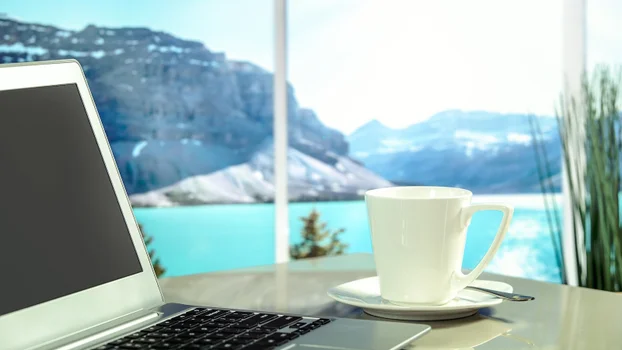 The view from a window looking over a lake and mountain with laptop in foreground.