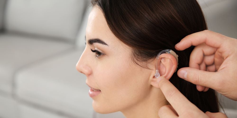 A person putting a hearing aid in a woman's ear