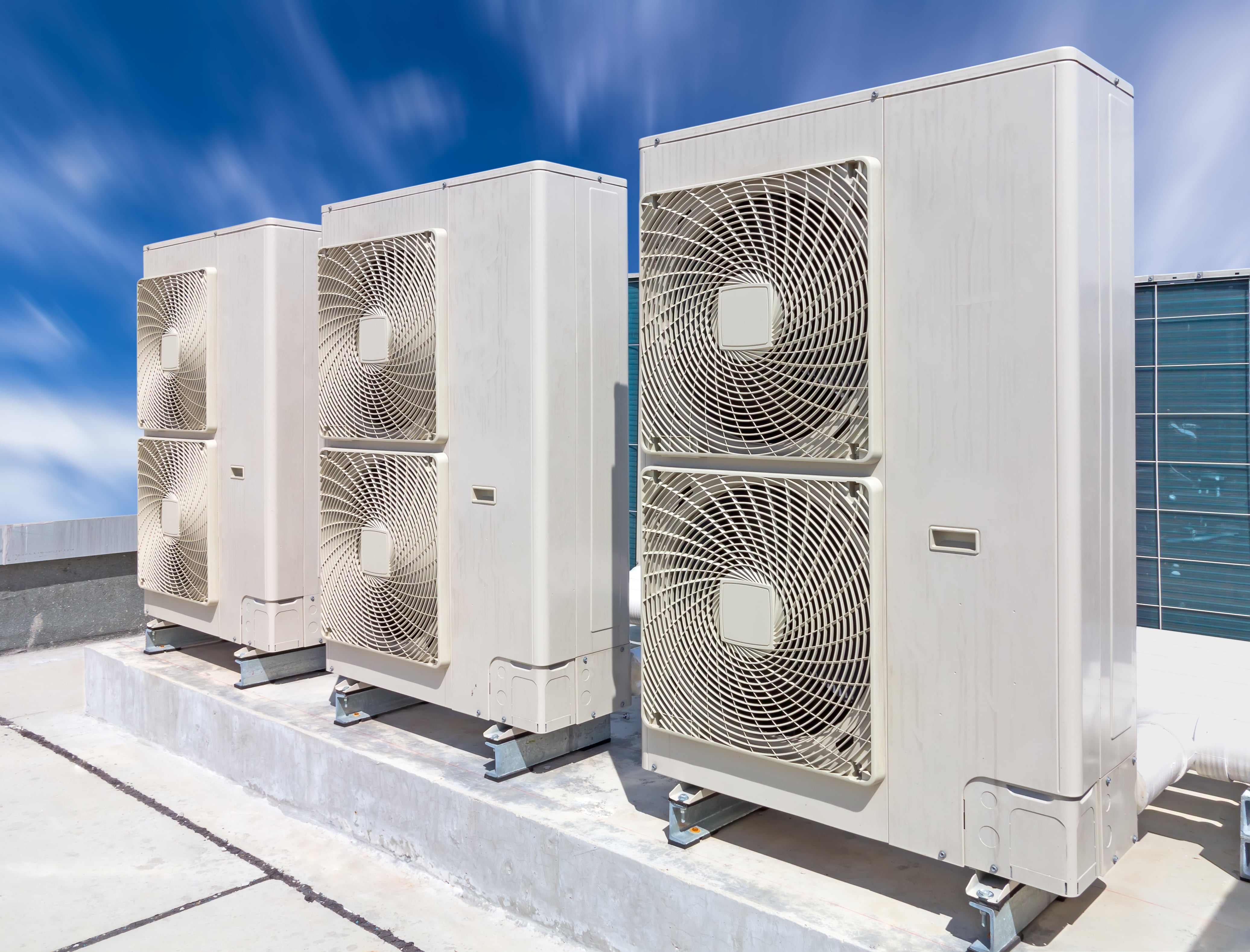Three large industrial HVAC units installed on a rooftop, featuring white casing and large fan grills, set against a clear blue sky.