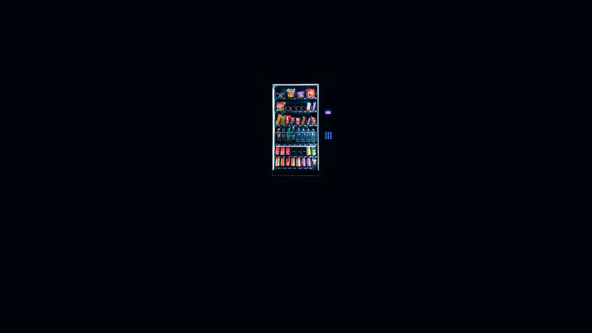 A single lit vending machine glowing in a dark room