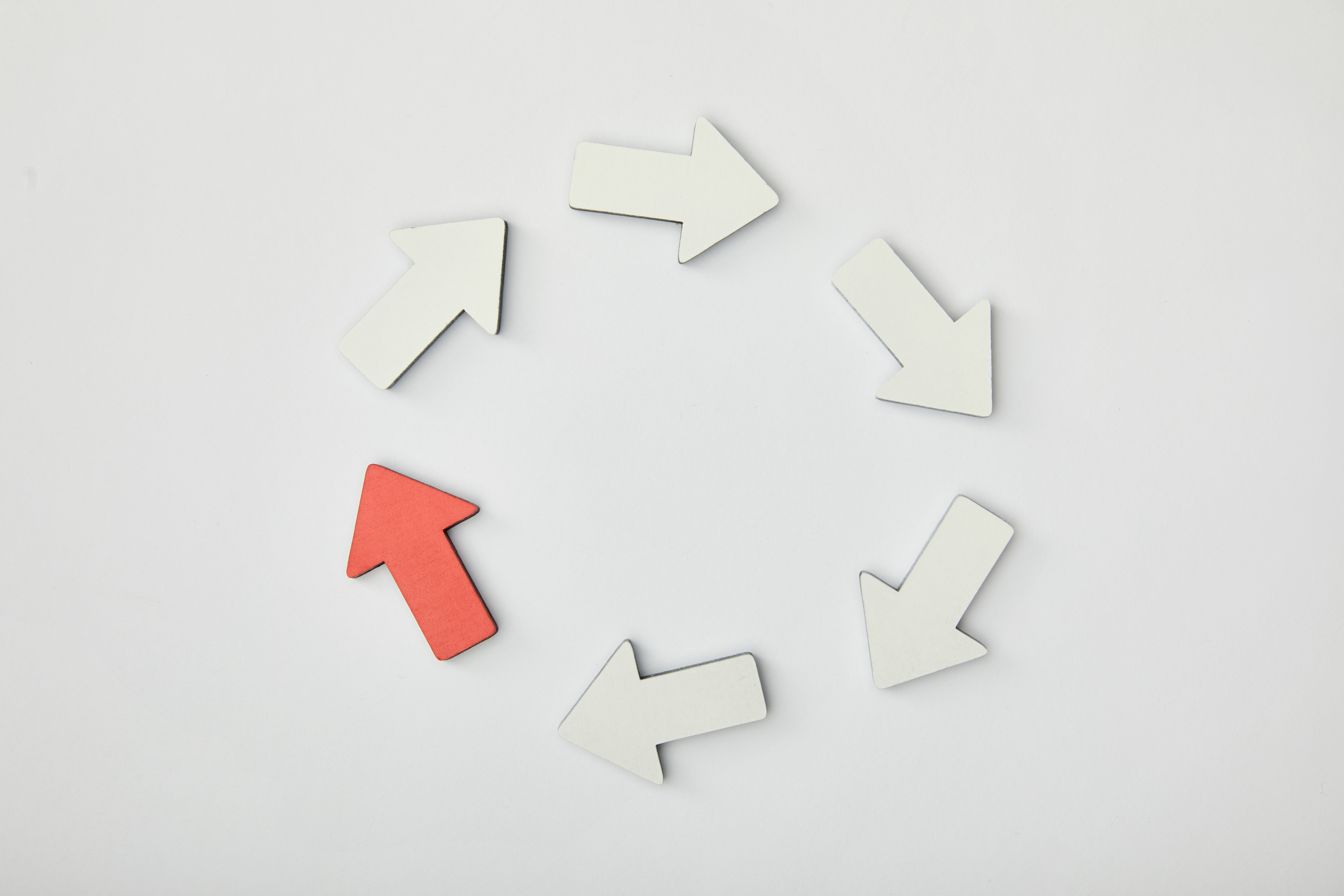Top view of white arrows and one red arrow pointing at each other to form a circle. 