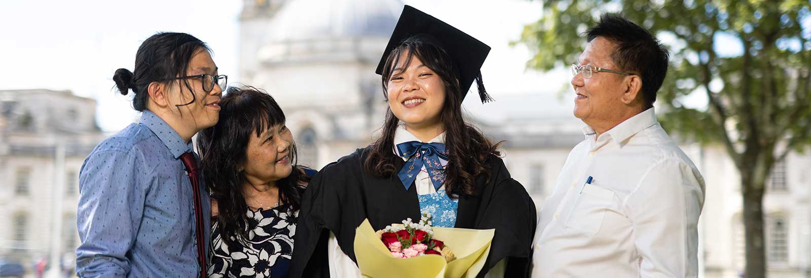 A graduate standing and smiling with family, holding flowers