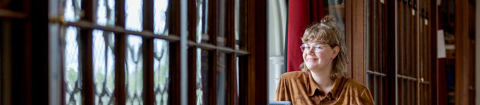 Student smiling and looking out window on campus