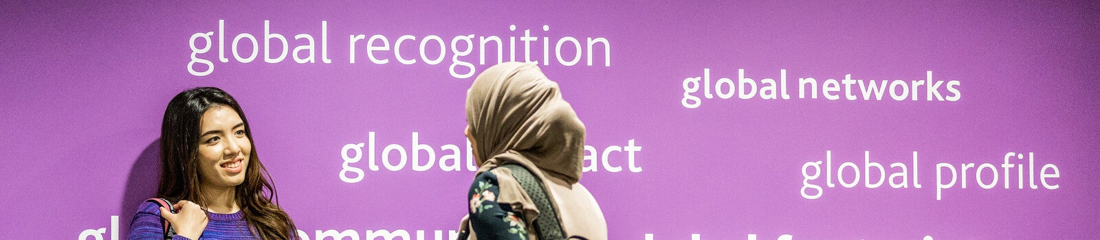 Two international students in front of a bright, purple wall