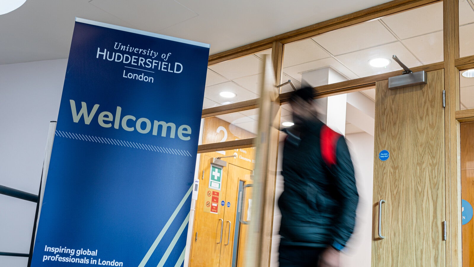 A blurred student walking past a Huddersfield London sign