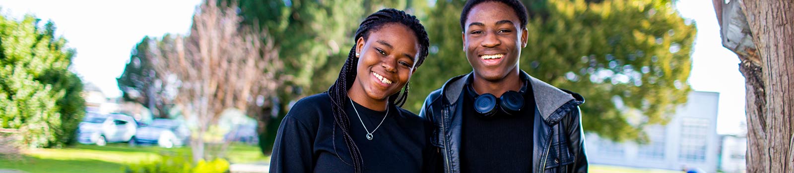 Two students smiling at the camera in front of green trees.