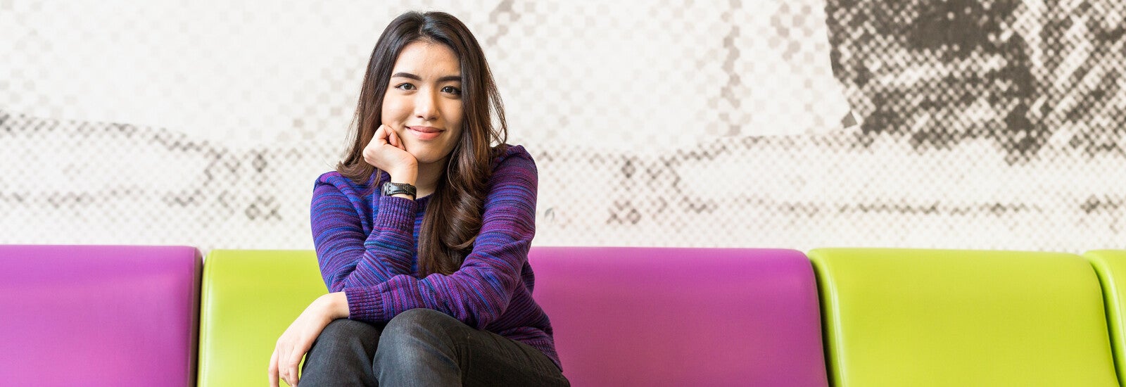 Student sitting on sofa on campus and smiling at camera