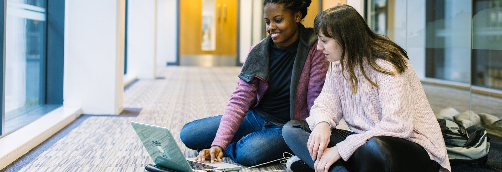 Two students sitting on the floor looking at a laptop