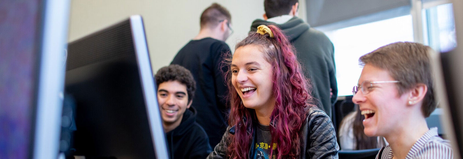 Three students laughing and using a computer