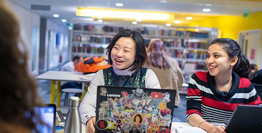 Students laughing and working on laptops in library