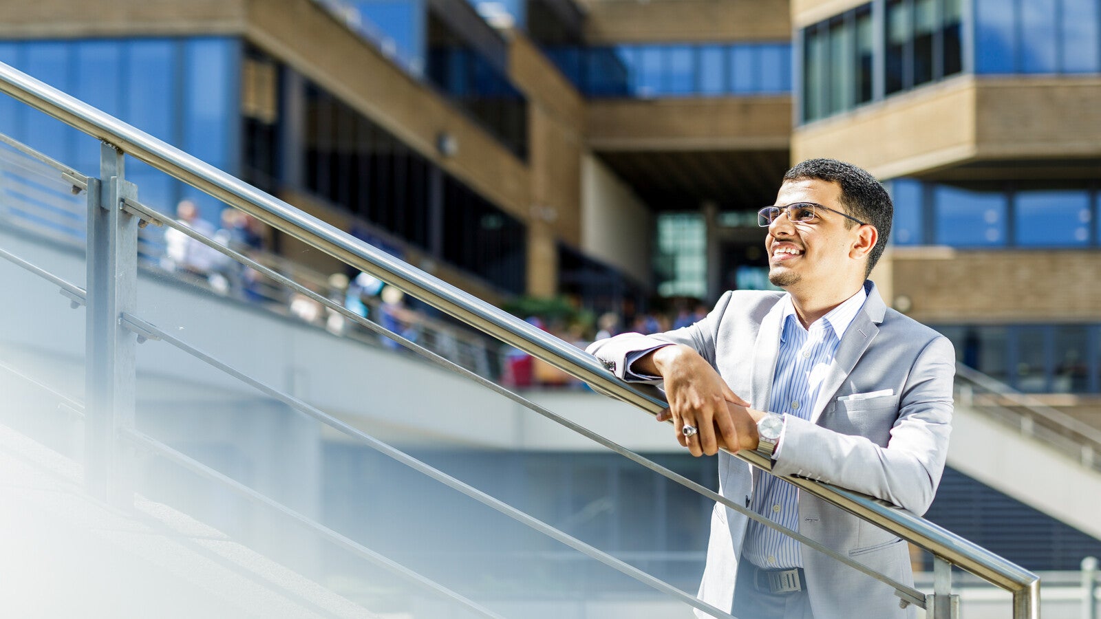 Student leaning on stair rail outside campus and smiling