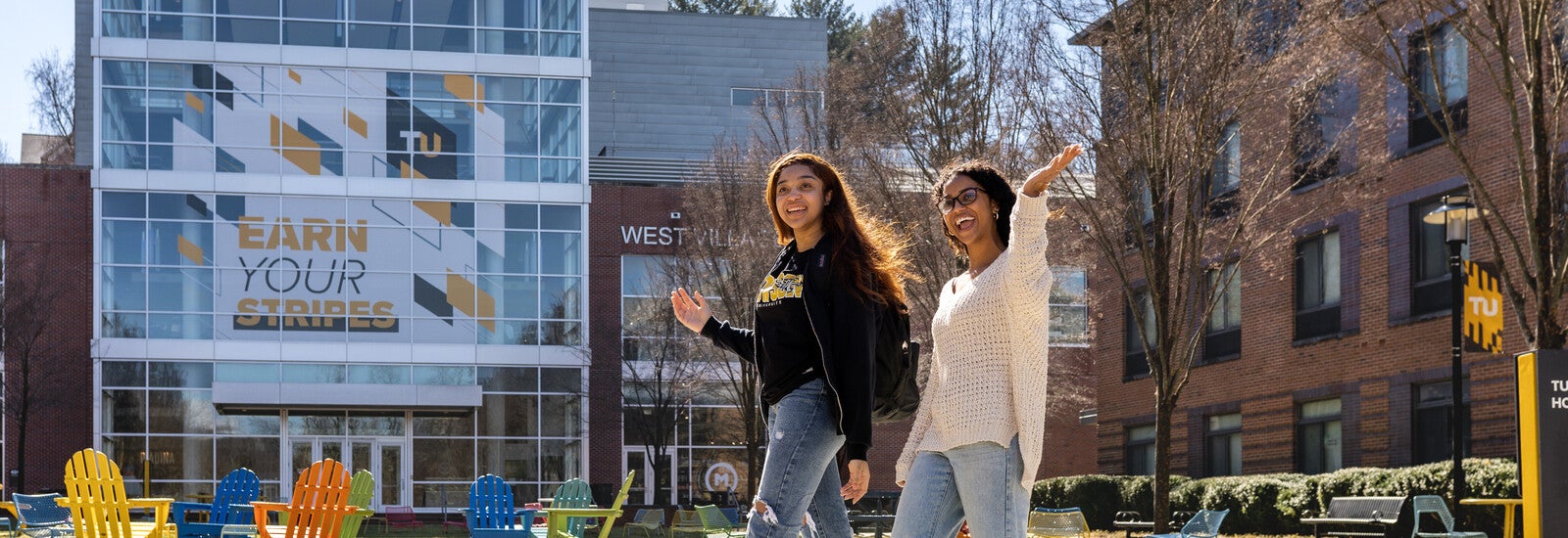 Two students smiling and waving outside campus