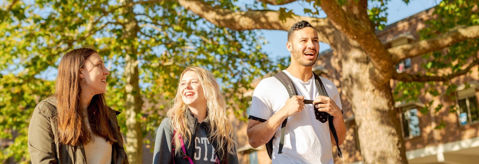 Three students smiling and walking in the sunshine.