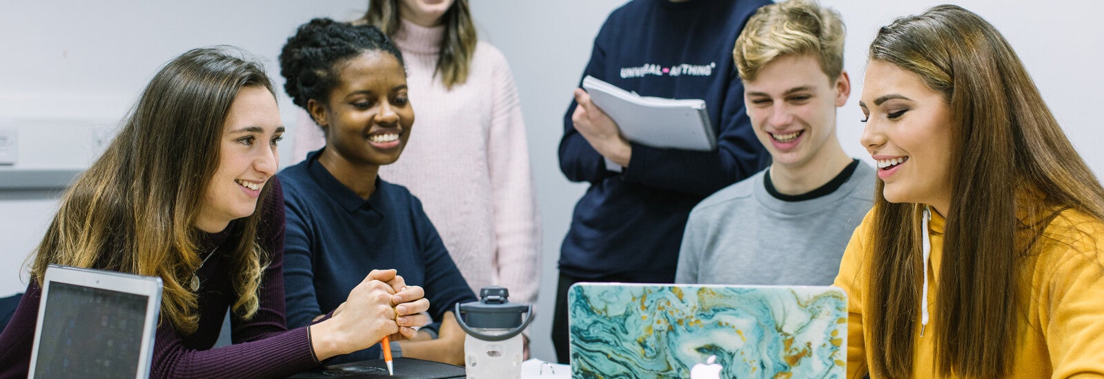 A group of students smiling and working on a laptop together