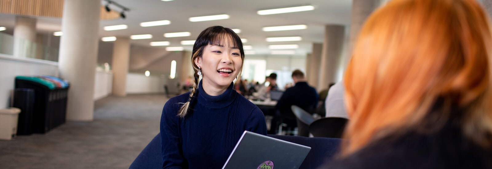 A student sitting inside and laughing, holding a laptop