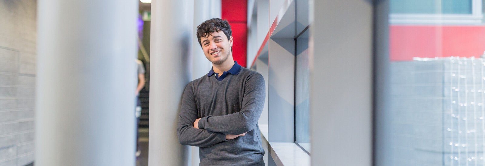 Student smiling and leaning against pillar on campus