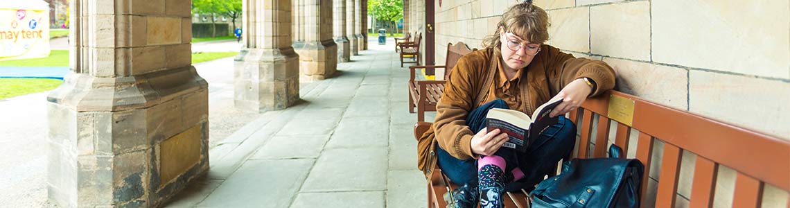 Student reading on bench outside campus