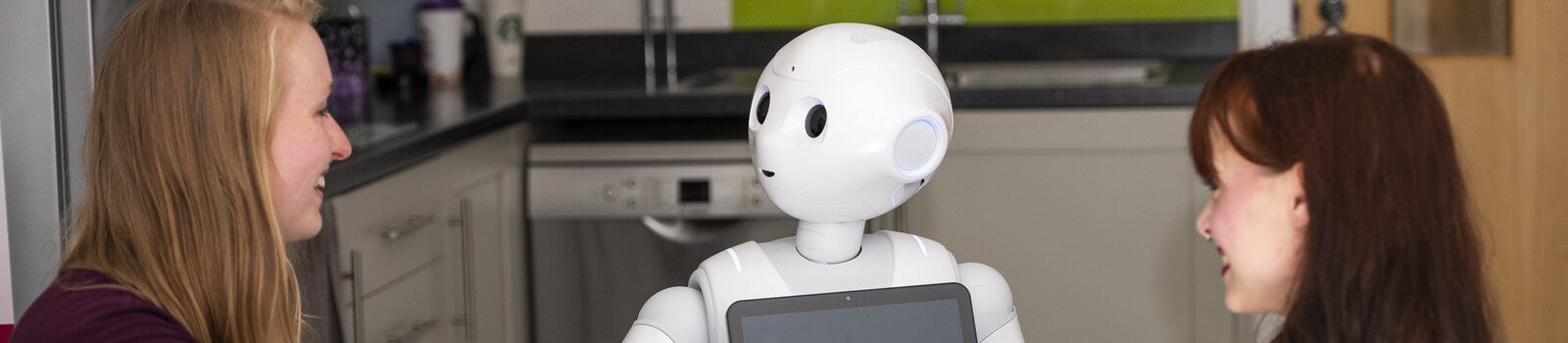 Two students sitting and smiling at a robot
