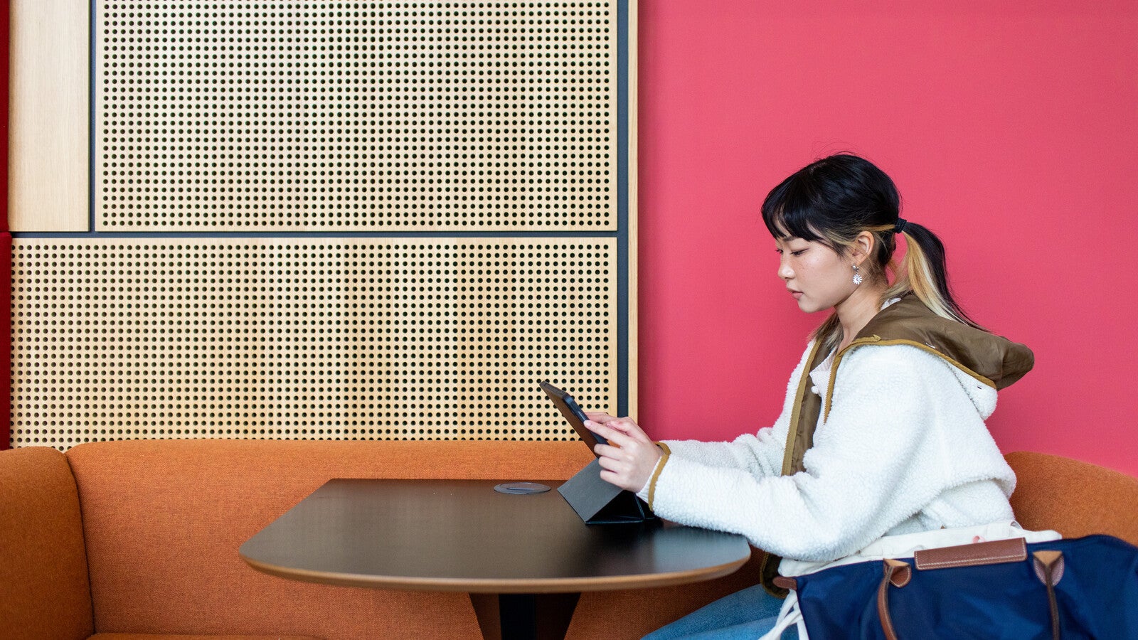 A student sitting at a table, looking at a tablet