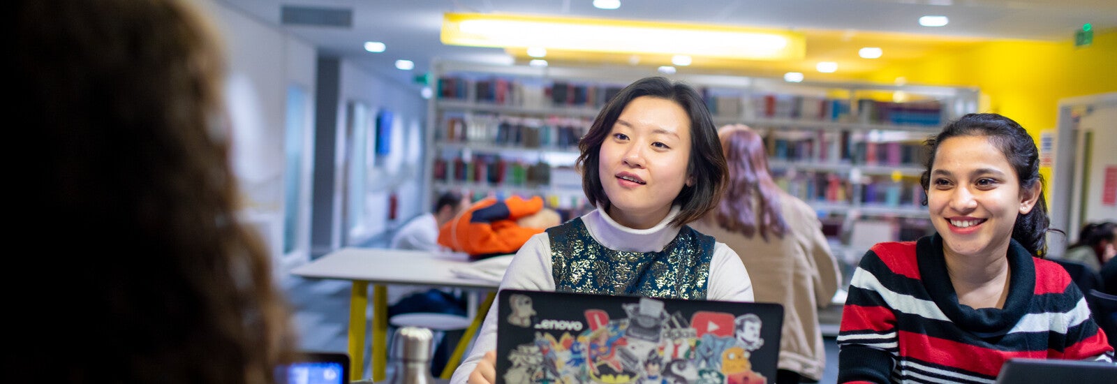 Students laughing and working on laptops in library