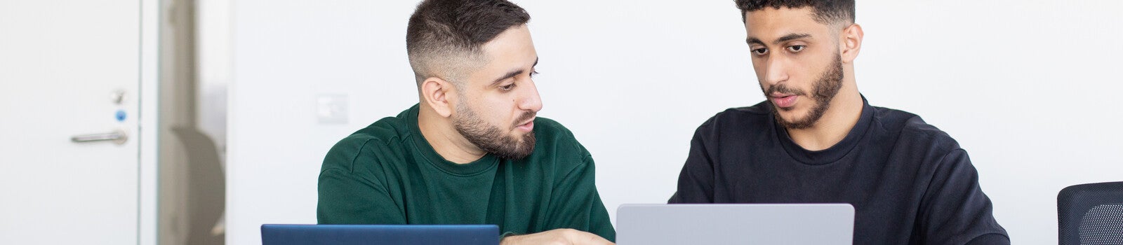 Two students talking and using laptops in class