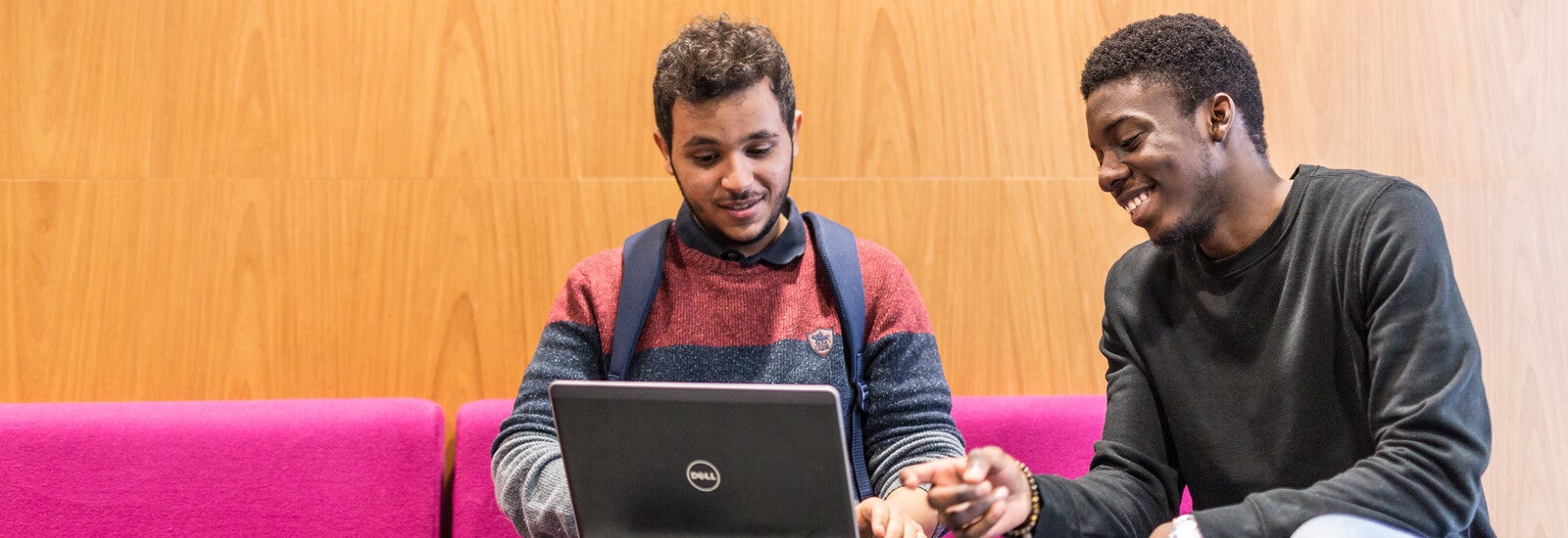 Two students sitting on a sofa, looking at a laptop