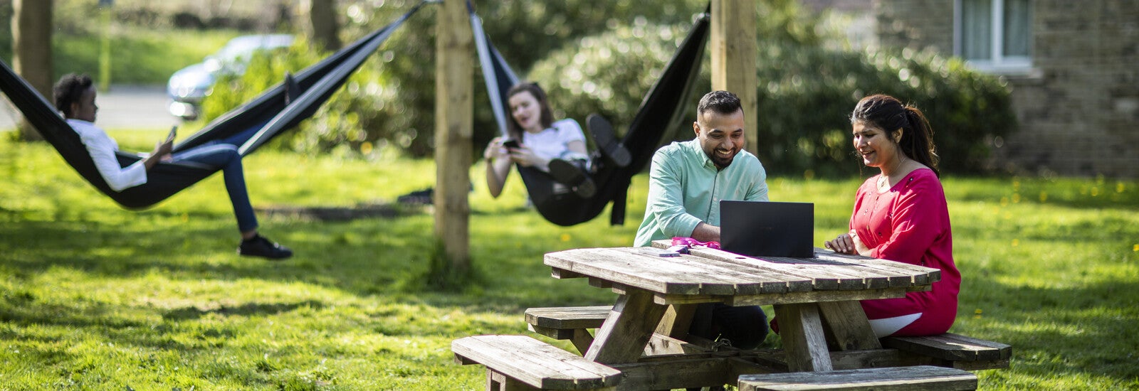 坐在校园外长凳上，使用笔记本电脑一起学习的学生