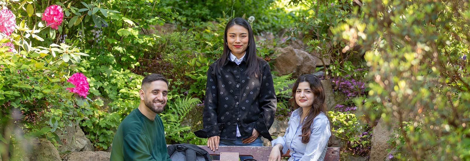 Three students smiling in front of rocks and plants