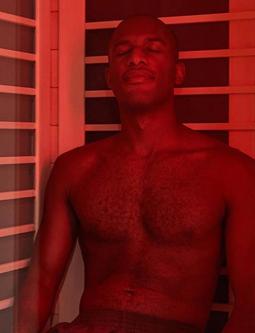 A man leans back and closes his in a Sunlighten Amplify sauna with red chromotherapy lights turned on. 