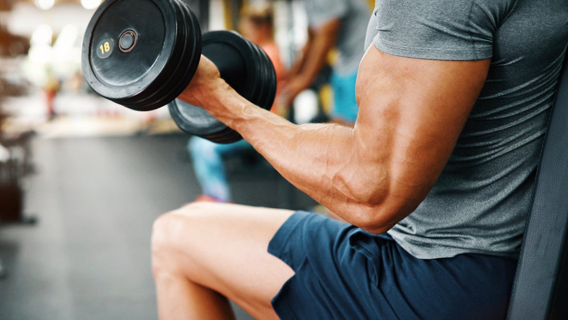 A man in a gym lifts a weight. 