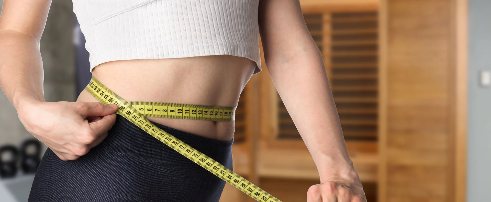 A fit person measuring their waist with a tape measure.