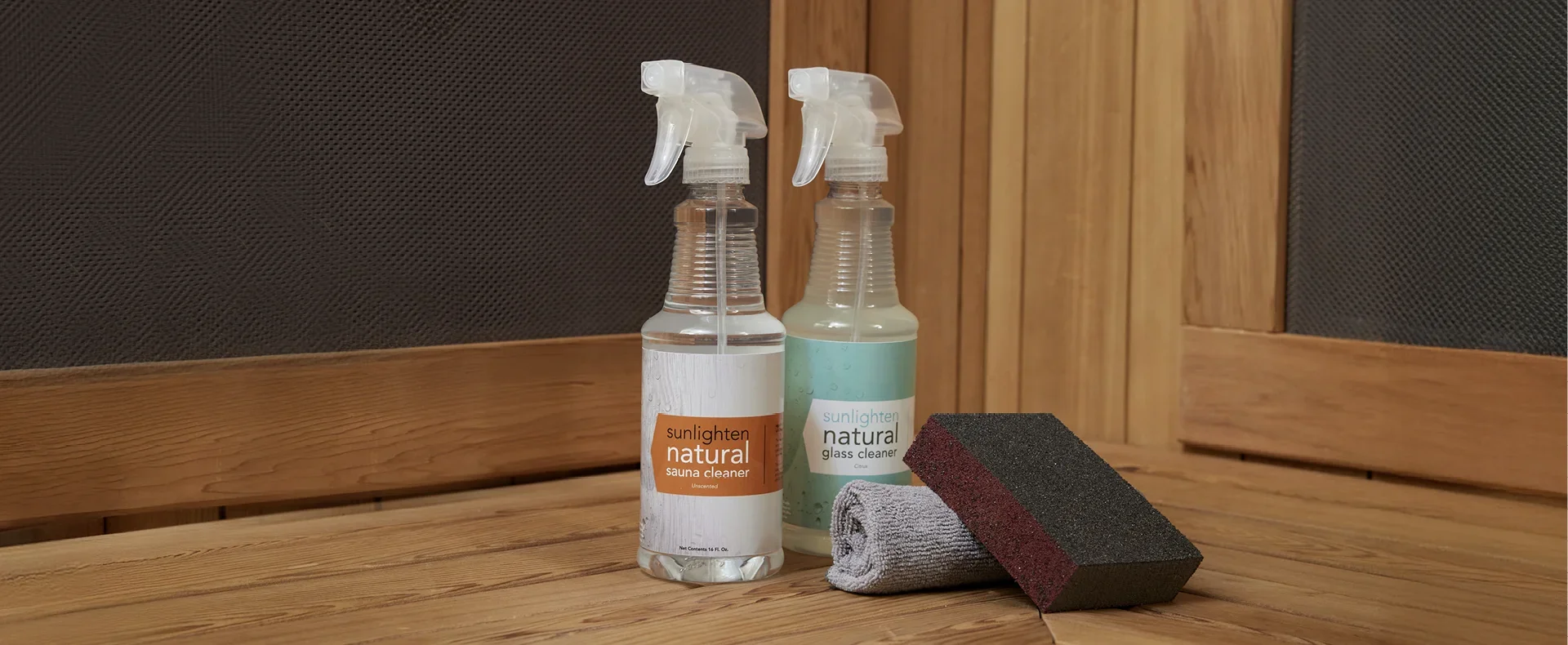 Sunlighten natural sauna cleaning products including sauna cleaner, glass cleaner, microfiber cloth, and sanding sponge inside a wood infrared sauna.