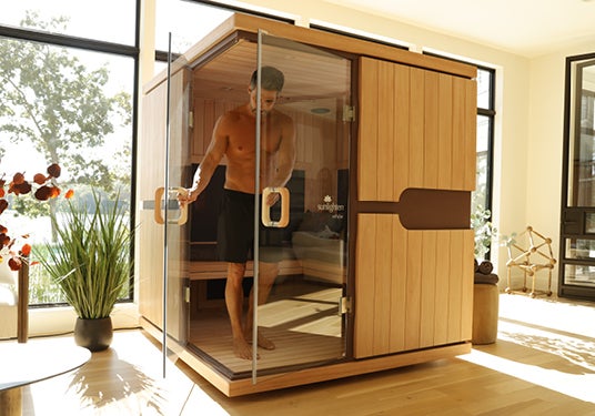 Man stepping into a Sunlighten home infrared sauna in a well-furnished sunny room