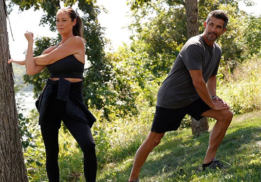 A man and woman stretch on a grassy hill. 