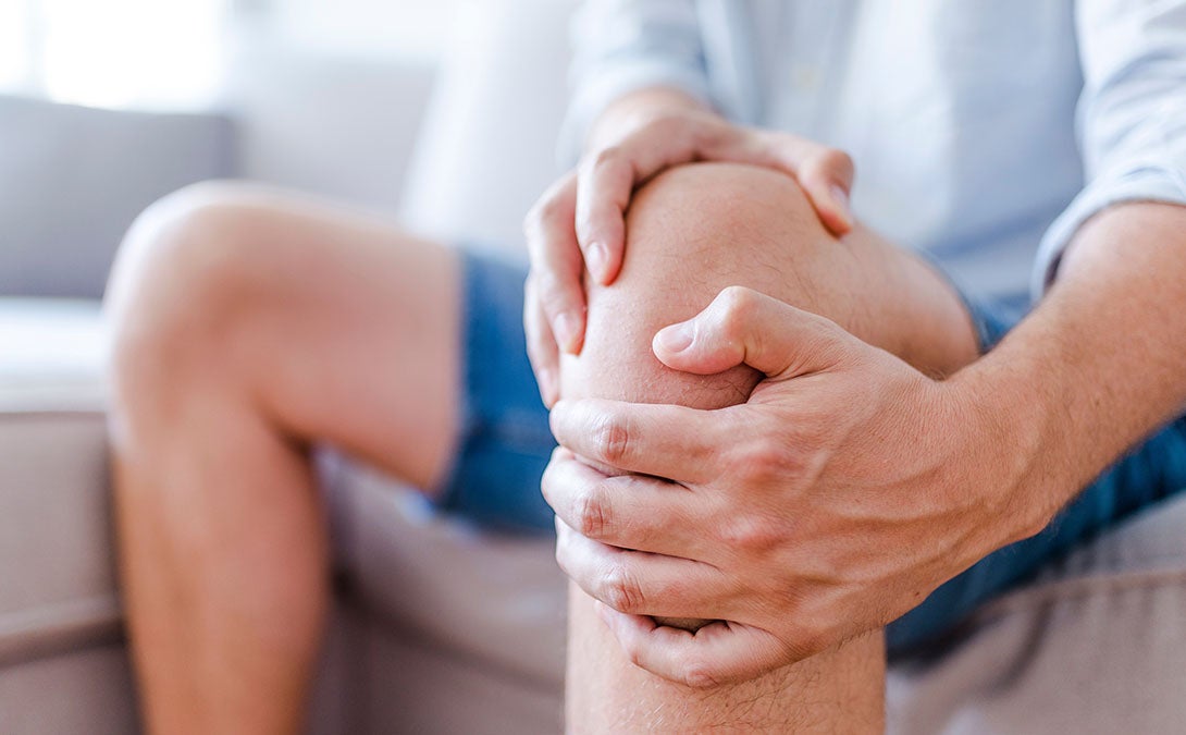A person seated, holding their knee and leg muscles in pain. 