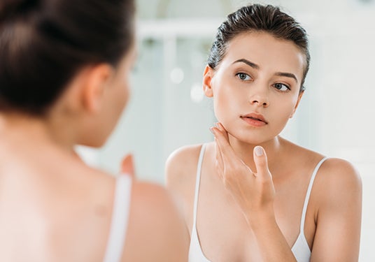 Woman looking at her skin in the mirror.