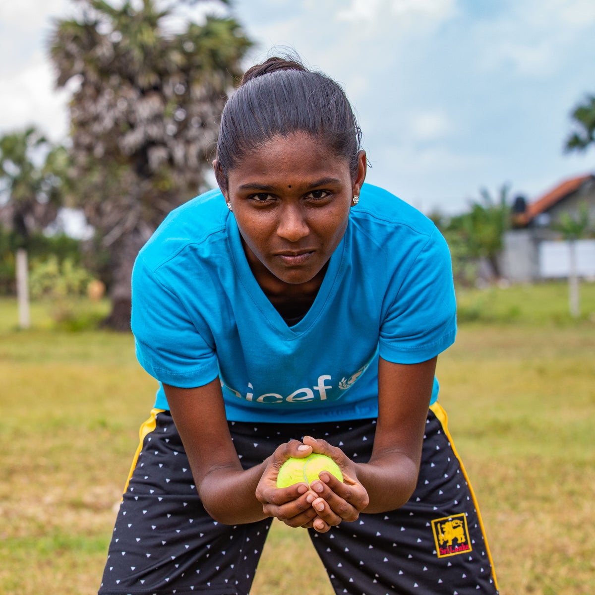 A young girl in Sri Lanka holding a ball during a cricket match.