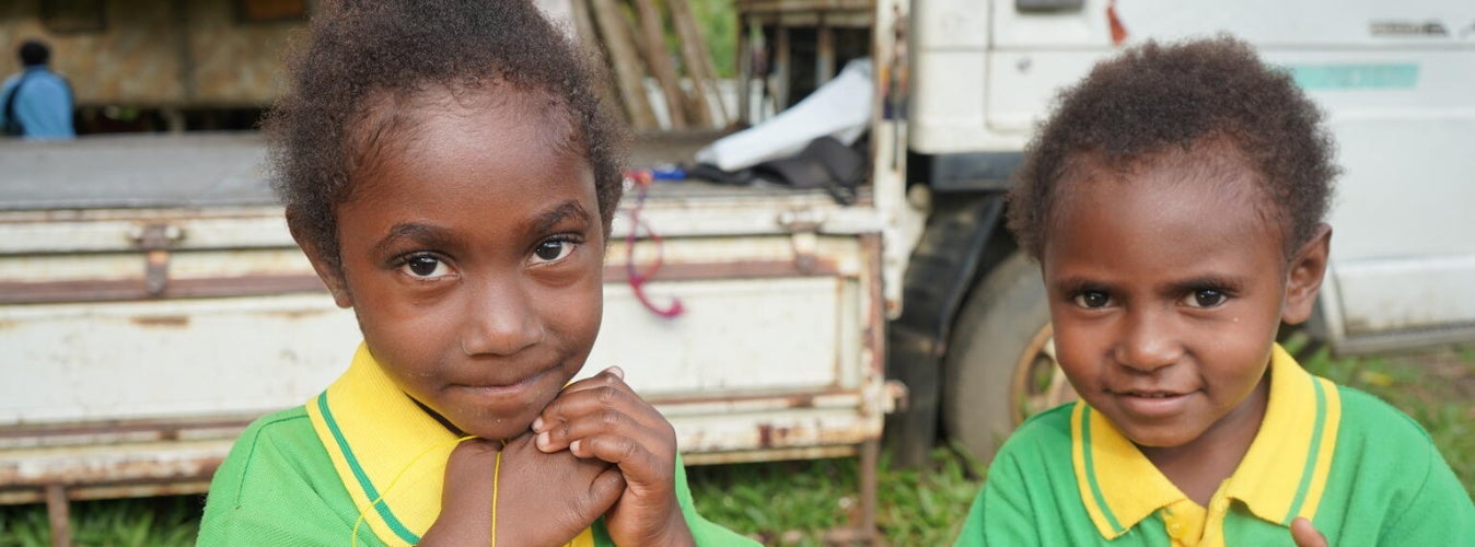 Two young children in a field next to a truck. 
