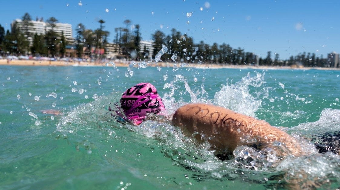 A woman with a pink swimming cap doing laps in the ocean.