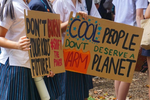 A group of school students at a climate protest hold up a sign saying ’Cool people don’t deserve a warm planet’.